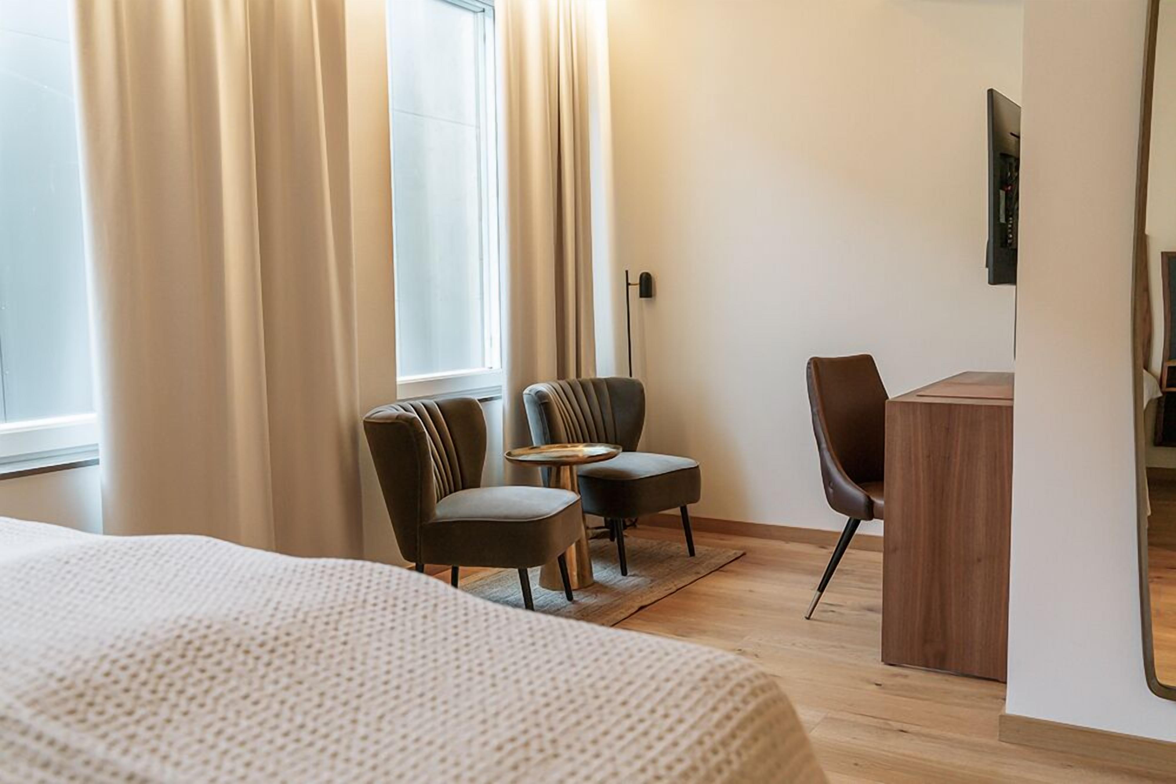 A hotel room with a large bed, two armchairs, a small table, and a wooden desk.