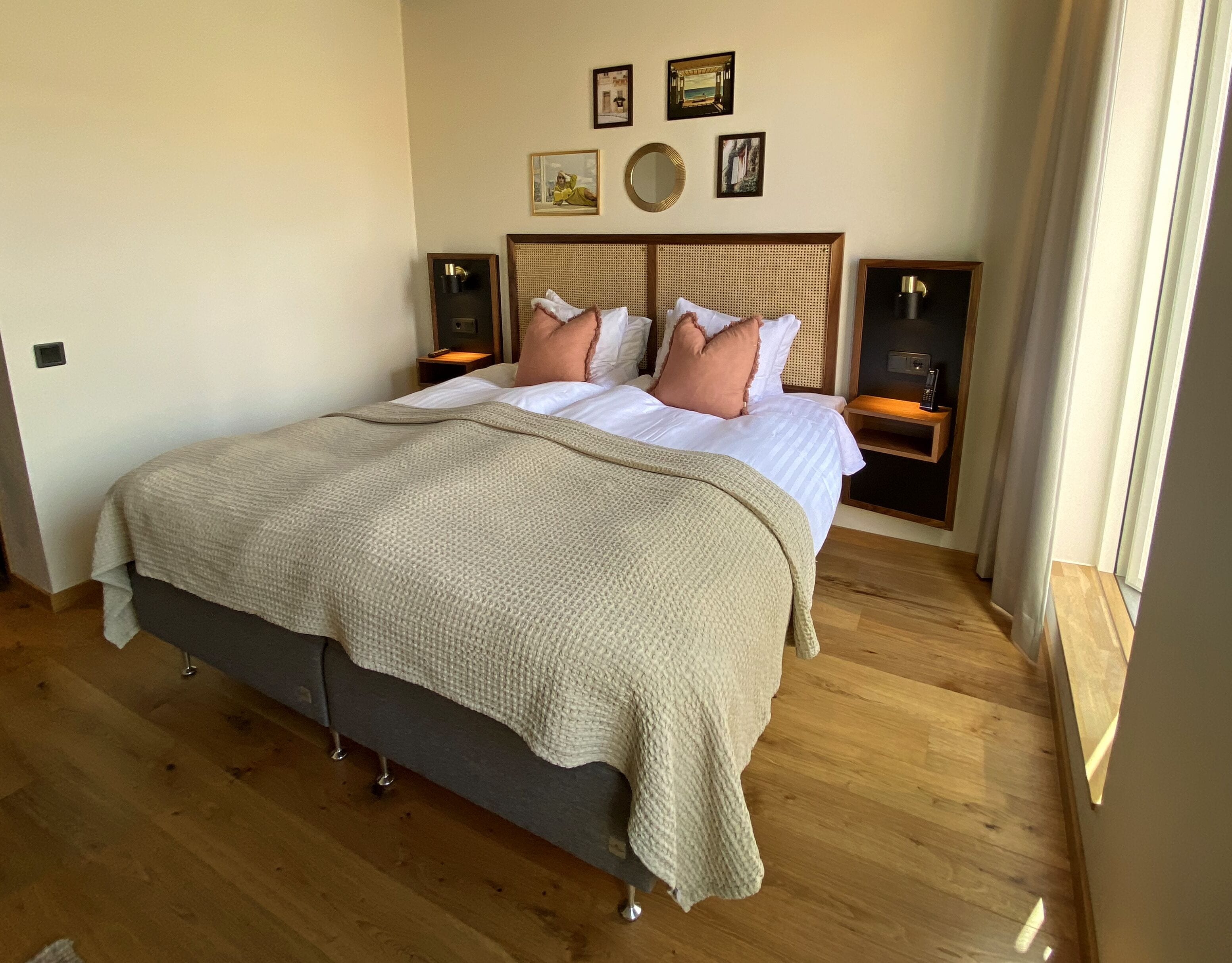 Una cama bien hecha con una manta color beige, dos mesitas de noche con lámparas y un cabecero de madera.