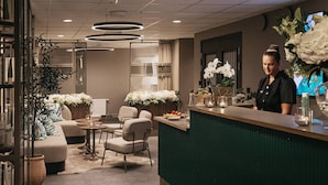 A modern hotel lobby with a reception desk, seating area, and decorative plants. - Fritiden Hotell & Kongress (Ystad)