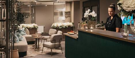 Un hall d’hôtel moderne avec un comptoir d’accueil, un espace salon et des plantes décoratives.
