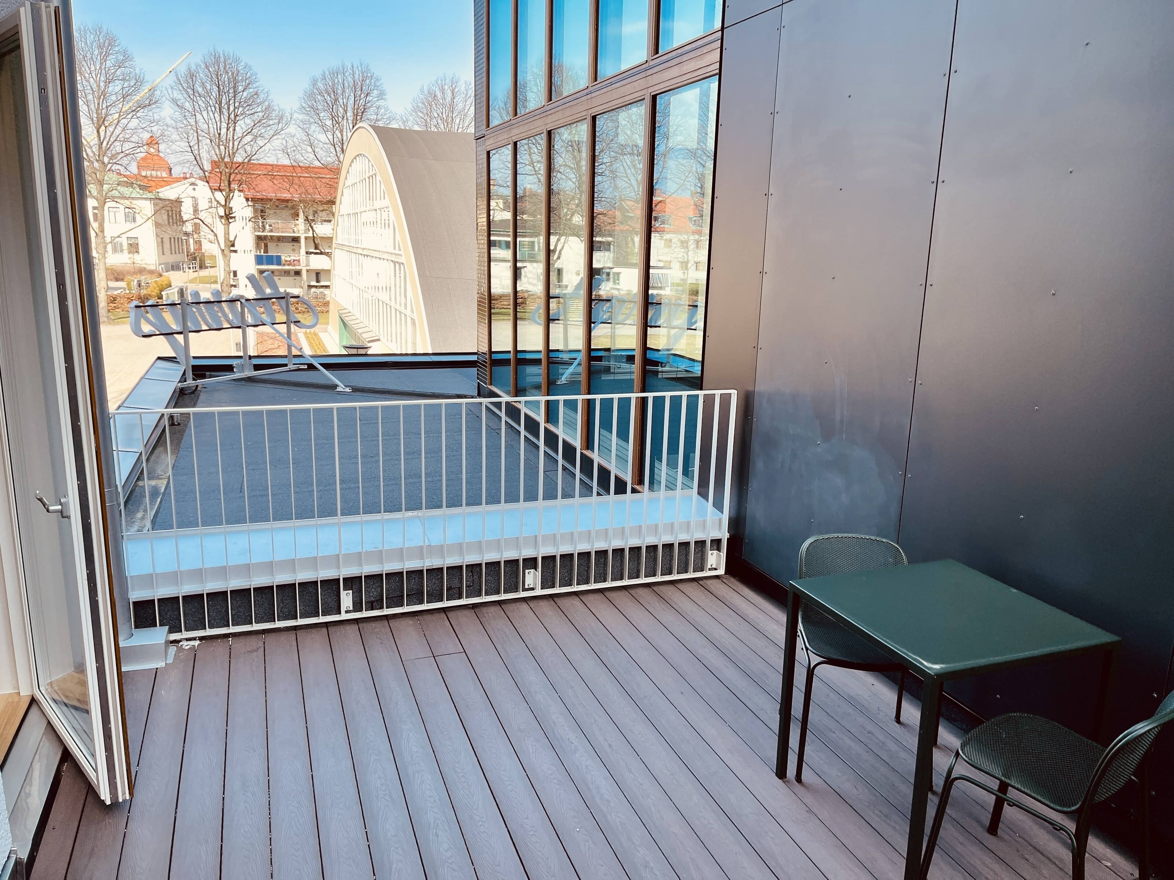 Een balkon met een metalen hekwerk, een klein tafeltje en een stoel.