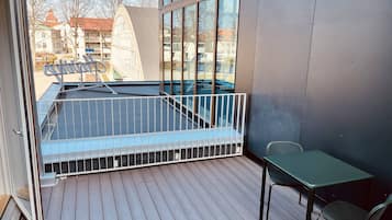 Een balkon met een metalen hekwerk, een klein tafeltje en een stoel.