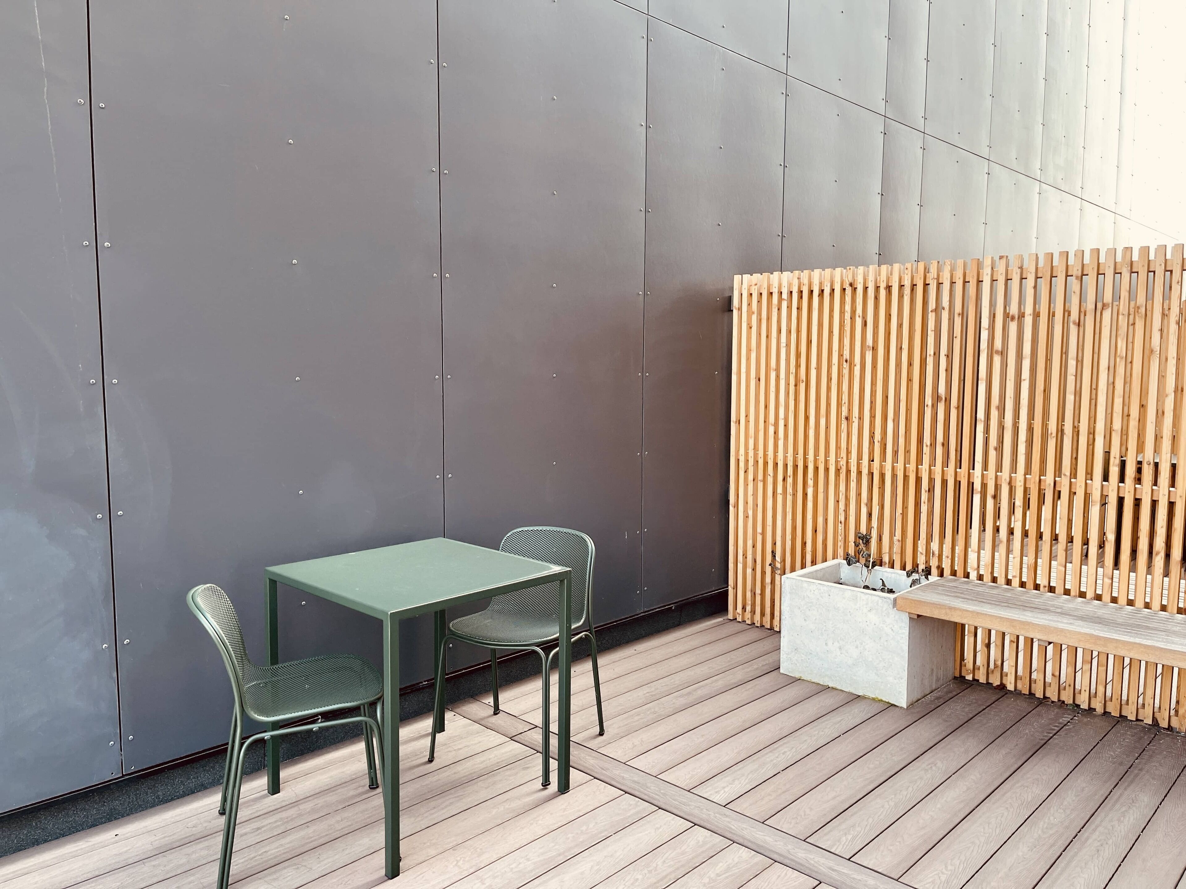 A modern outdoor seating area with a table and chairs, a wooden fence, and a bench.