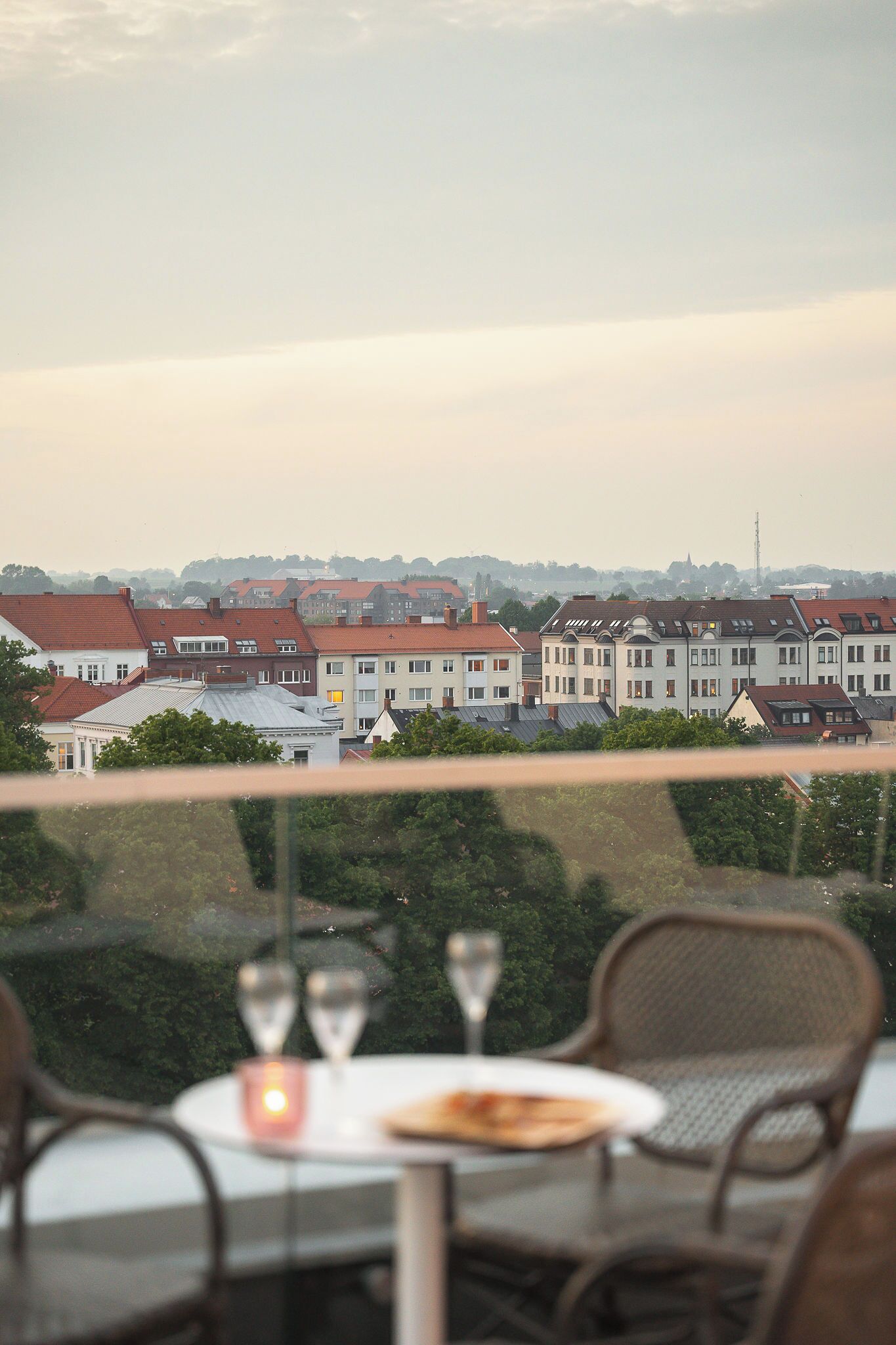 A dining area with a table and chairs, overlooking a row of buildings with red roofs.