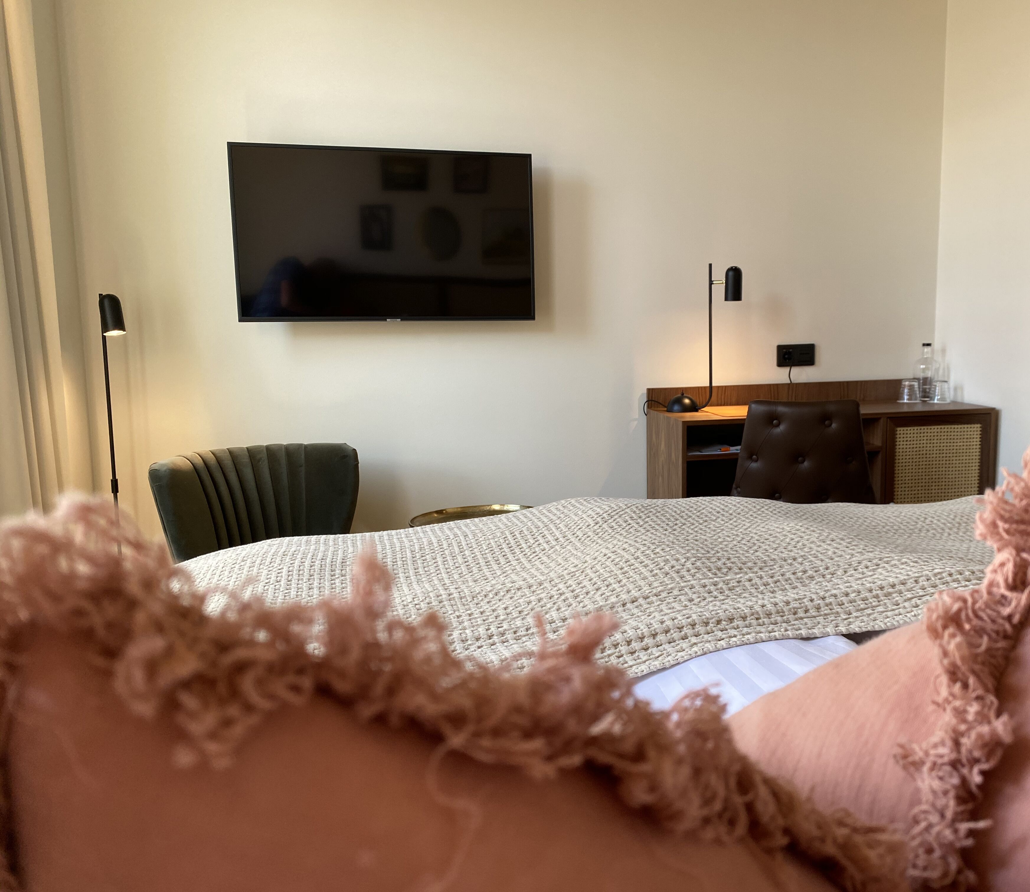 Una camera d'albergo con un letto, una scrivania, una sedia e una televisione appesa al muro.