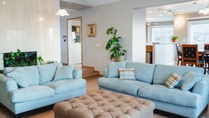 Una sala de estar moderna con dos sofás azul claro, un otoman beige y una planta grande en maceta.