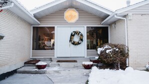 Una casa con puerta blanca, un adorno de lazo y nieve en el suelo.