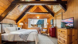 Um quarto de sótão aconchegante com cama, cômoda, televisão e janela com vista.