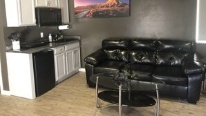 A compact living space with a kitchenette, a black leather sofa, and a glass coffee table. - Modern Studio excellent location. (Grand Junction)