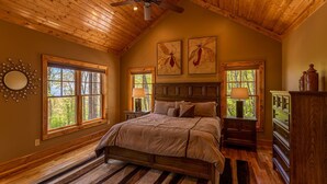 Ein Schlafzimmer mit Holzboden, einem Bett, zwei Fenstern und einer Kommode.