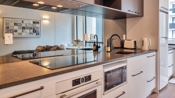 A modern kitchen with a central island, built-in oven, and stainless steel appliances. - Chic Metro Apartment with Free Parking and Air-con (Auckland CBD)