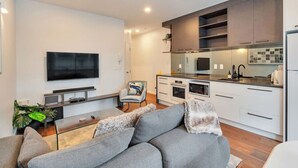 A modern living room with a grey sofa, a flat-screen TV, and a small coffee table. - Chic Metro Apartment with Free Parking and Air-con (Auckland CBD)