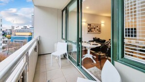 A balcony with a view of the city, a dining area with a table and chairs, and a sofa. - Chic Metro Apartment with Free Parking and Air-con (Auckland CBD)
