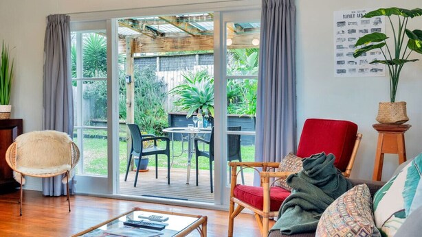A living room with a glass door leading to a patio, a red chair, a wicker chair, and a sofa with patterned cushions.