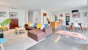Uma sala de estar moderna com um sofá marrom, uma mesa de centro e uma área de jantar com cadeiras brancas e uma mesa pequena.