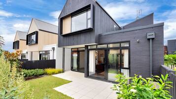 A modern two-story house with a large glass door entrance, a well-maintained garden, and a clear sky.