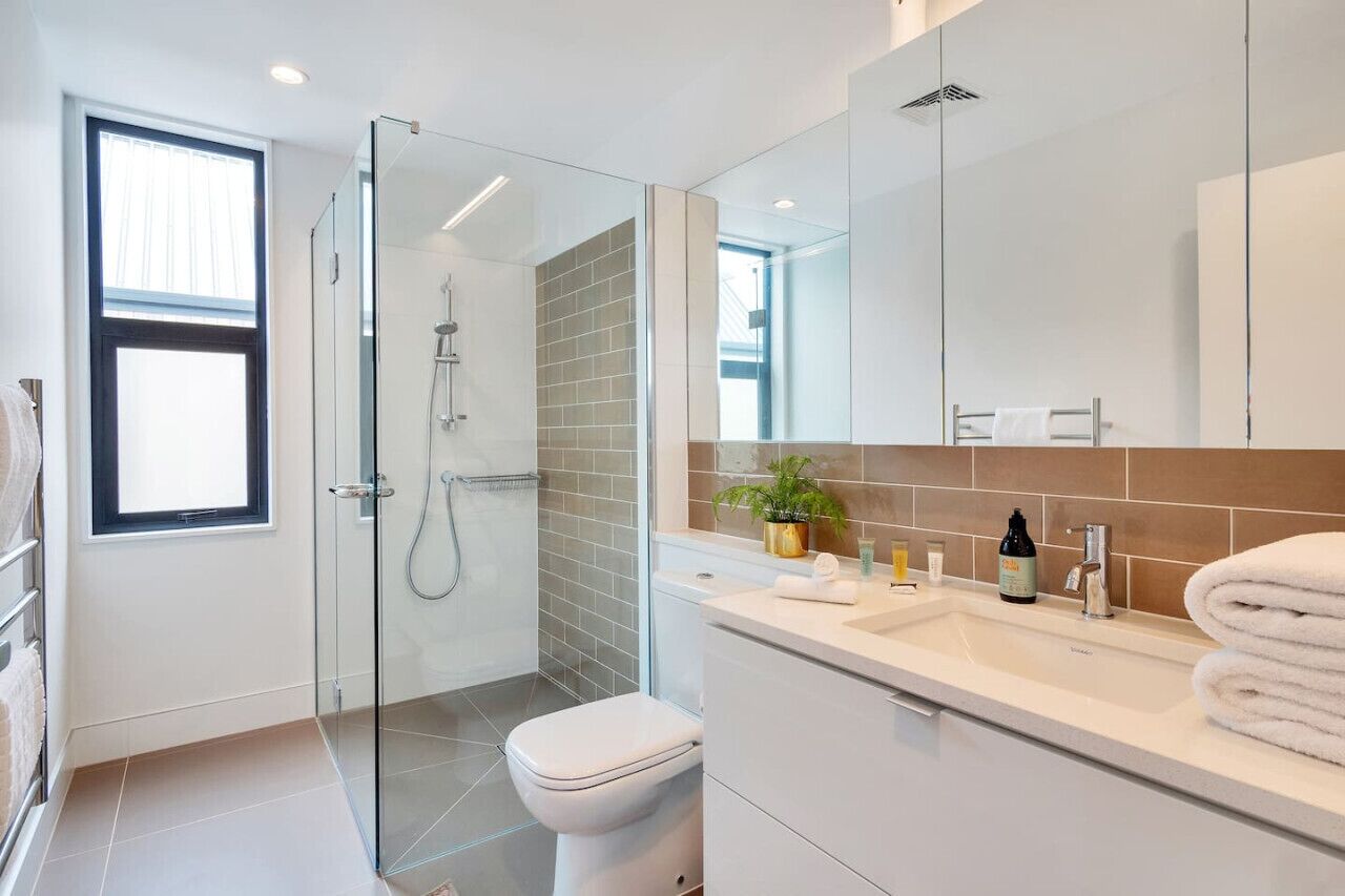 A modern bathroom with a glass shower enclosure, a white toilet, and a vanity with a mirror and sink.