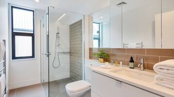 A modern bathroom with a glass shower enclosure, a white toilet, and a vanity with a mirror and sink.