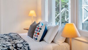 A neatly made bed with patterned bedding, a bedside lamp, and a window with a view of greenery. - Classic Villa Retreat - Steps To Ponsonby Rd (Auckland Central Suburbs)