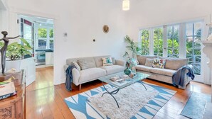 A spacious living room with a large window, a sofa, a coffee table, and a decorative plant. - Classic Villa Retreat - Steps To Ponsonby Rd (Auckland Central Suburbs)