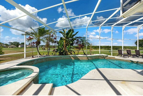 A swimming pool with a clear blue water, surrounded by a white fence, and various tropical plants.