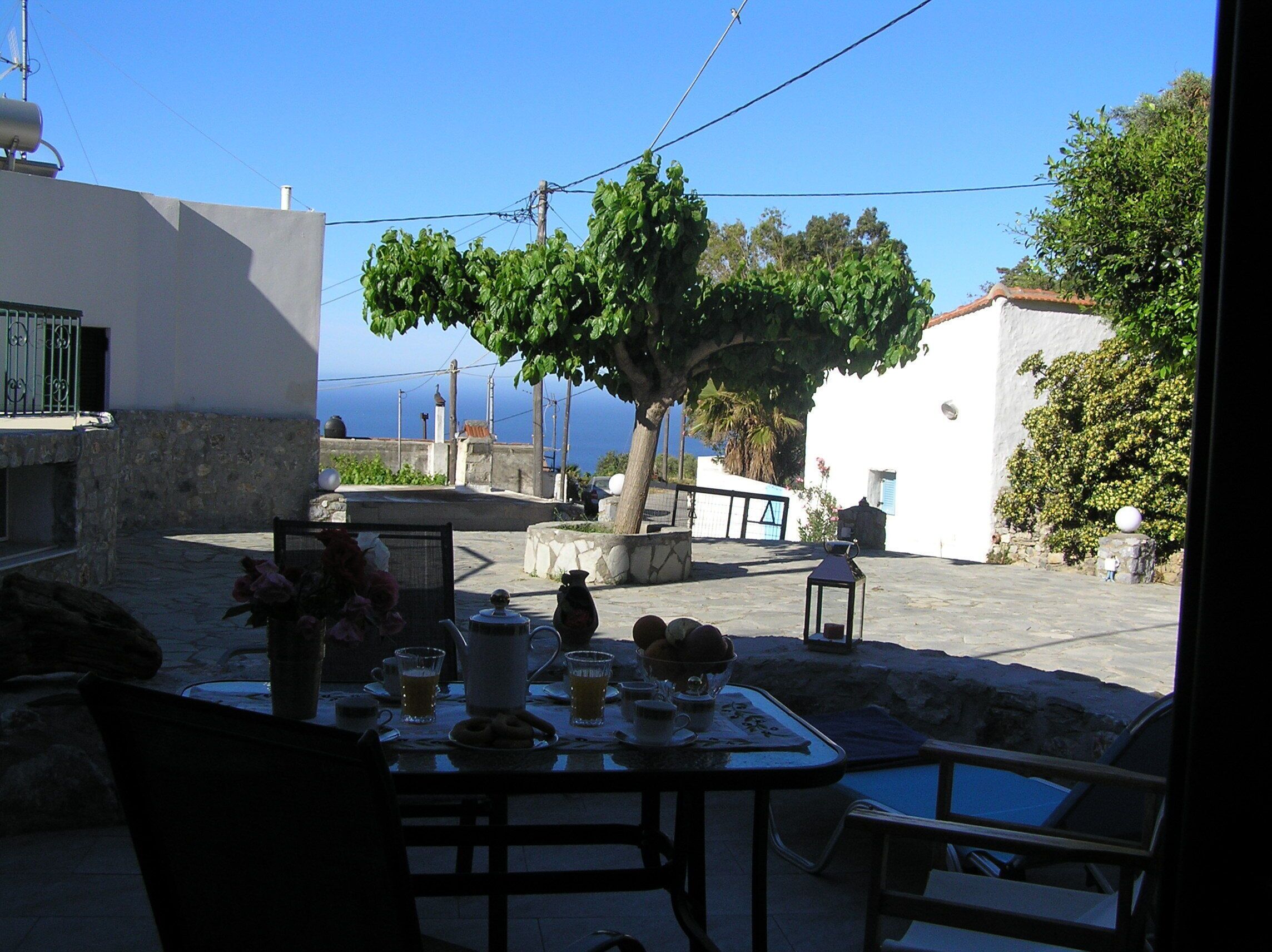 Une table dressée à l’extérieur, avec vue sur la mer, entourée d’immeubles et d’un arbre.