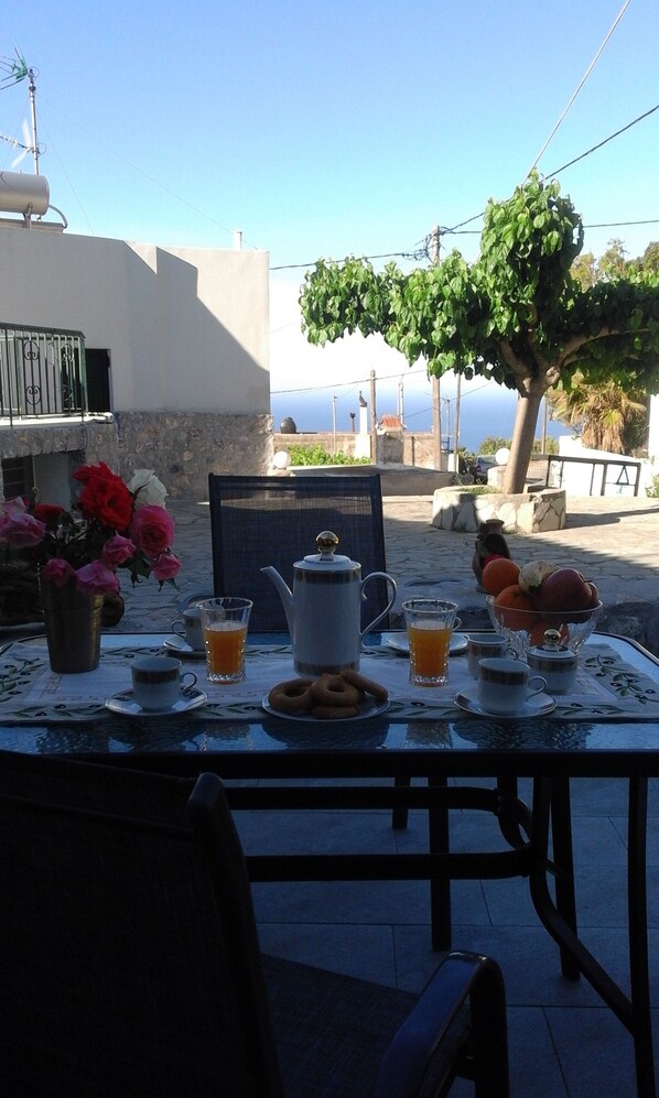 A table set for breakfast with a view of the sea, a flower vase, and a tree.