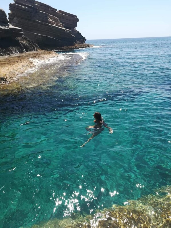 A swimmer in clear blue water near rocky cliffs.