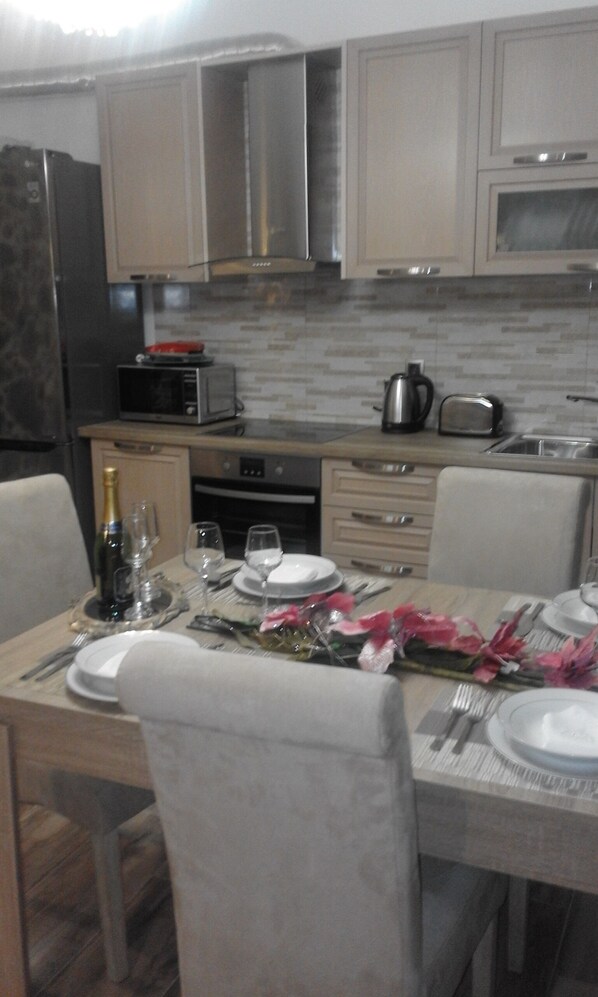 Un coin repas avec une table dressée pour deux personnes, un four à micro-ondes, un grille-pain et un réfrigérateur en arrière-plan.