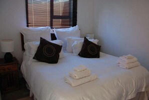 A neatly made bed with white linens, two decorative pillows, and folded towels on the bed. - D & H Guesthouse (Graskop)