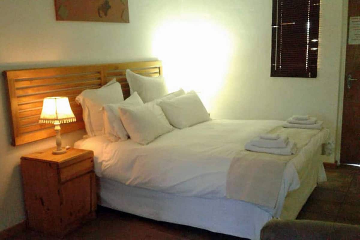 A neatly made bed with white linens and pillows, a bedside lamp, and a wooden nightstand.