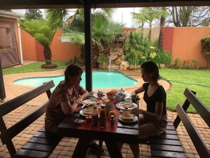 An outdoor dining area with a pool, surrounded by greenery and a stone wall. - D & H Guesthouse (Graskop)