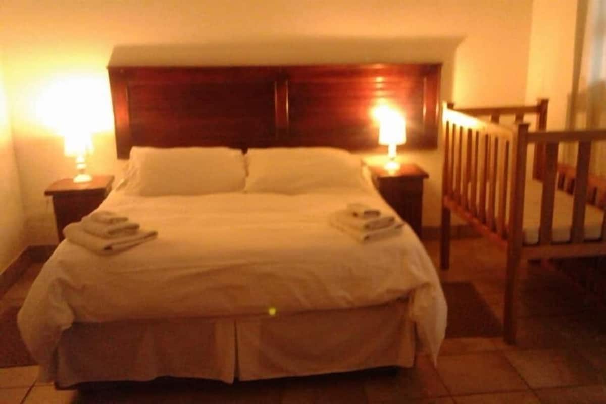 A hotel room with a large bed, two bedside tables, a wooden chair, and a nightstand with a lamp.
