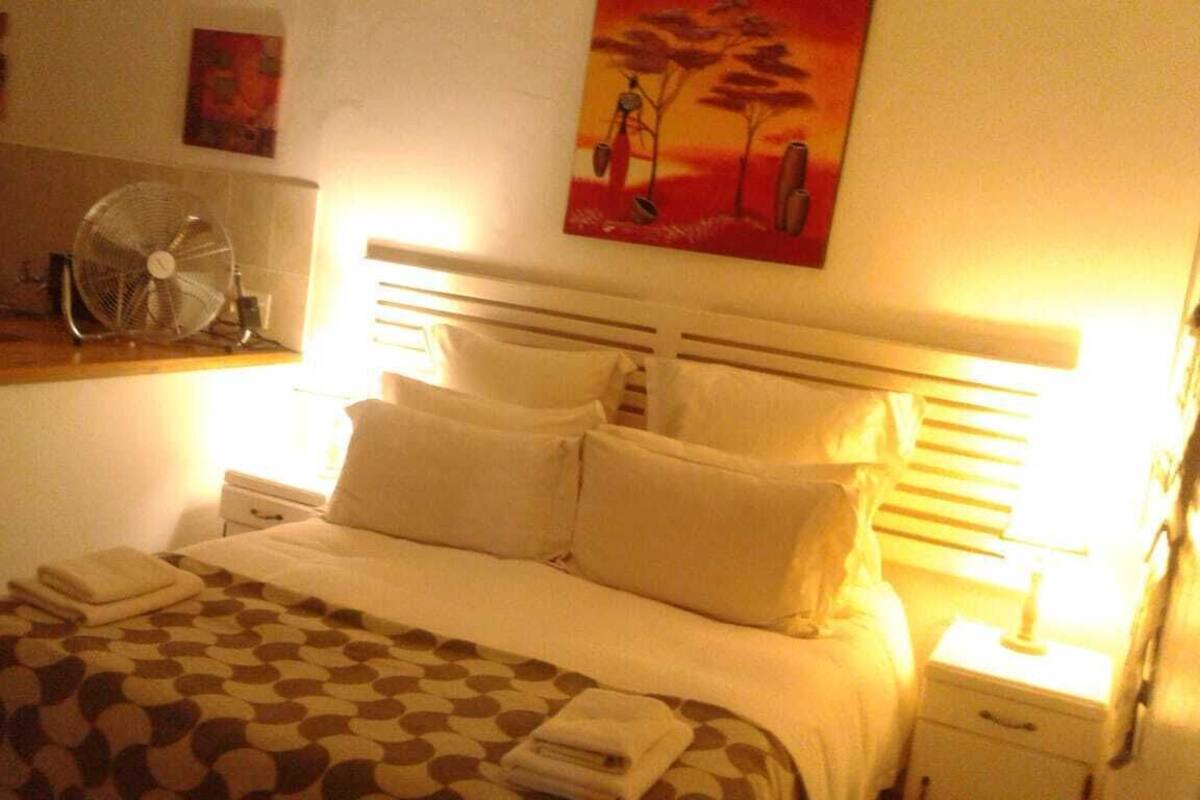 A neatly made bed with white linens, a patterned throw, and a bedside table with a lamp.