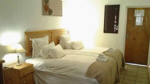 A bedroom with two beds, a wooden headboard, a bedside lamp, a wooden cabinet, and a door with a window.