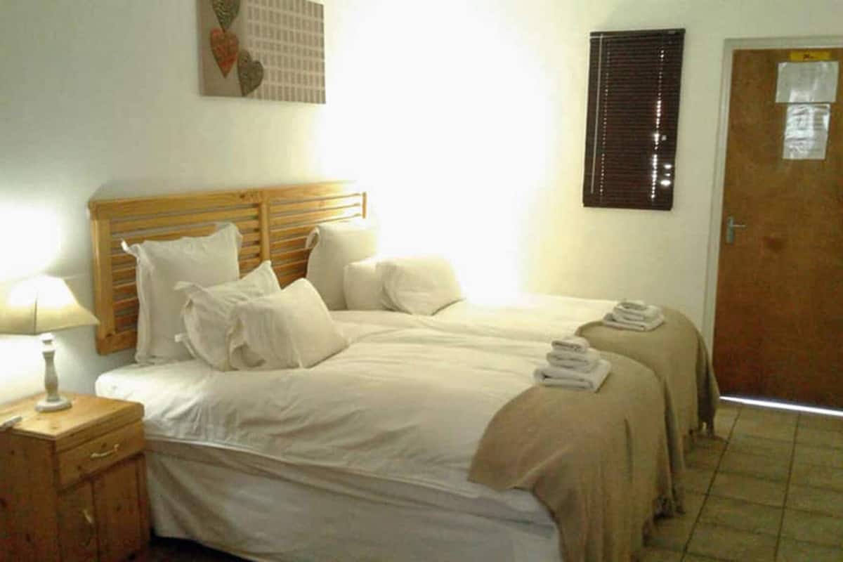 A bedroom with two beds, a wooden headboard, a bedside lamp, a wooden cabinet, and a door with a window.