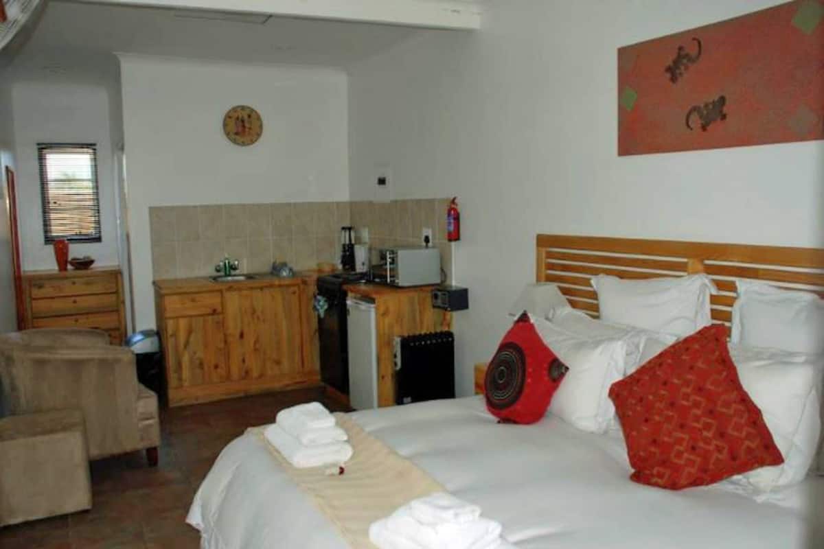 A hotel room with a bed, a wooden desk, a kitchenette, and a bathroom.