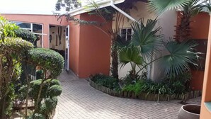 A paved courtyard with a brick pathway, surrounded by various plants and a large planter.