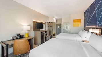 A hotel room with two beds, a desk with a chair, a TV, a coffee maker, and a wardrobe.