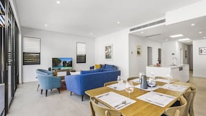 A modern living room with a blue sofa, a dining table set for two, and a kitchen area in the background.