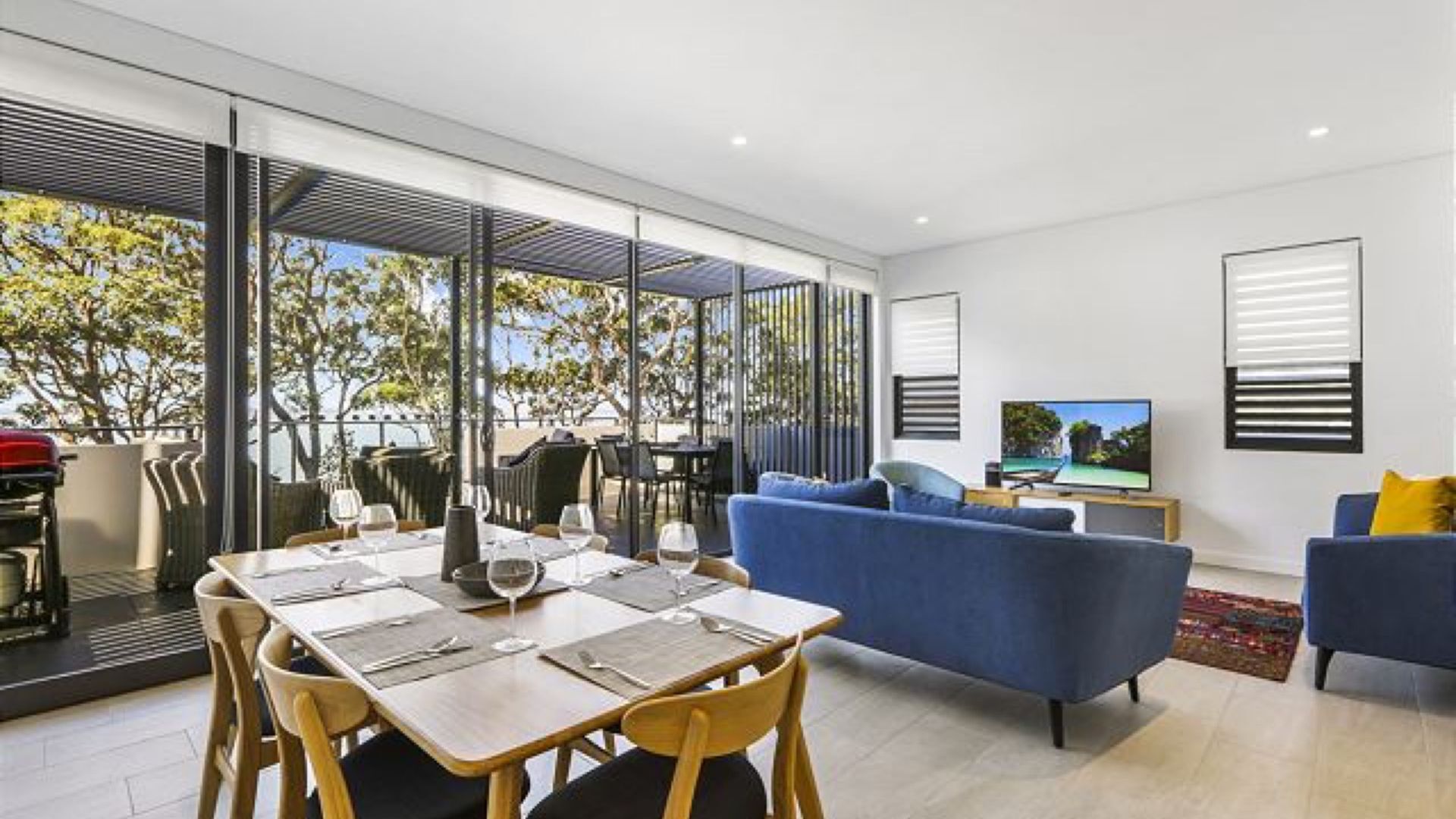 A modern living room with a dining area, large windows, and a flat-screen TV.