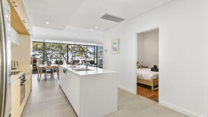A modern kitchen with a central island, a dining area with chairs, and a bedroom with a bed and nightstand.