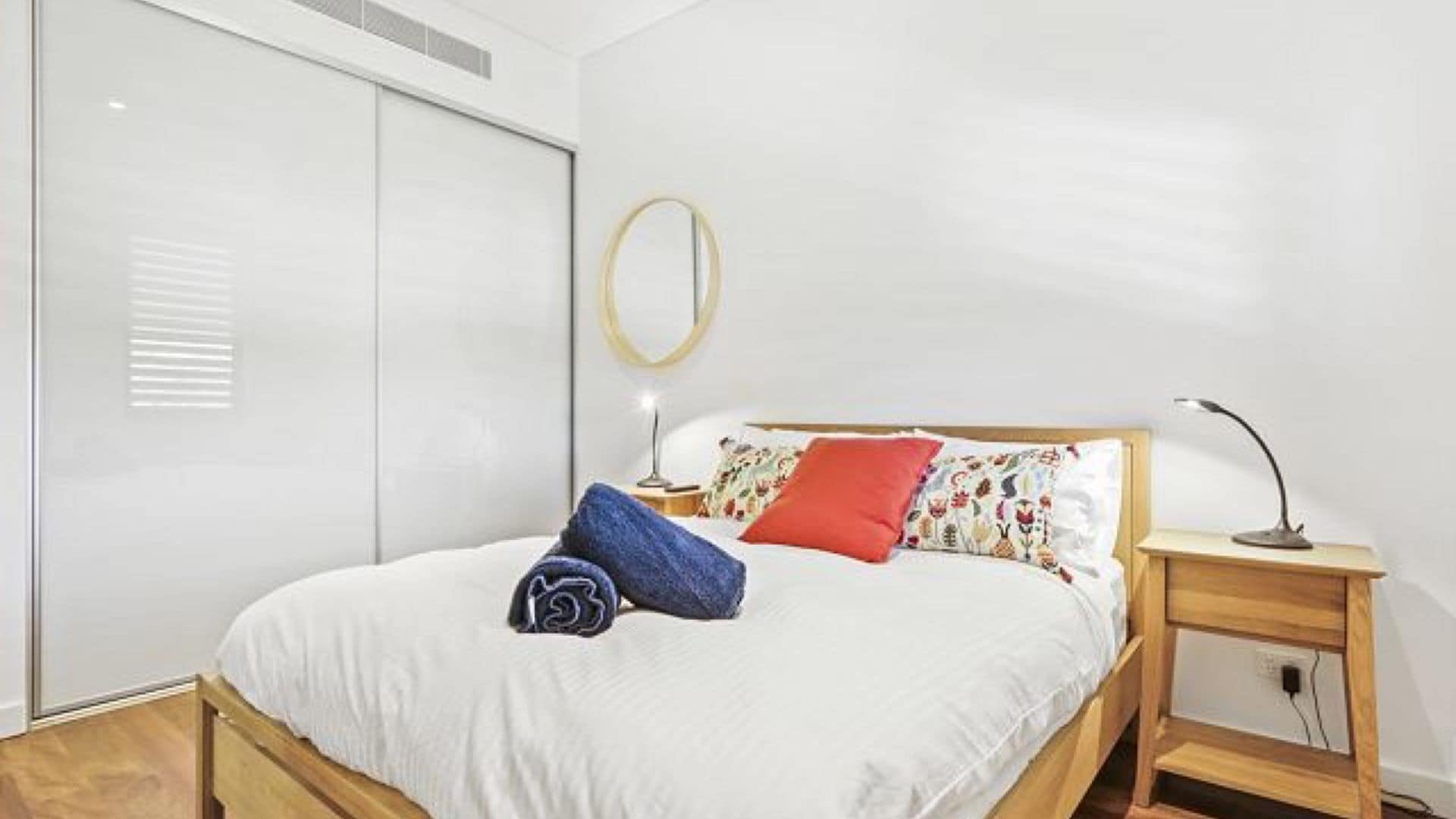 Une chambre à coucher avec un lit, une table de chevet avec une lampe, une armoire et un miroir rond accroché au mur.