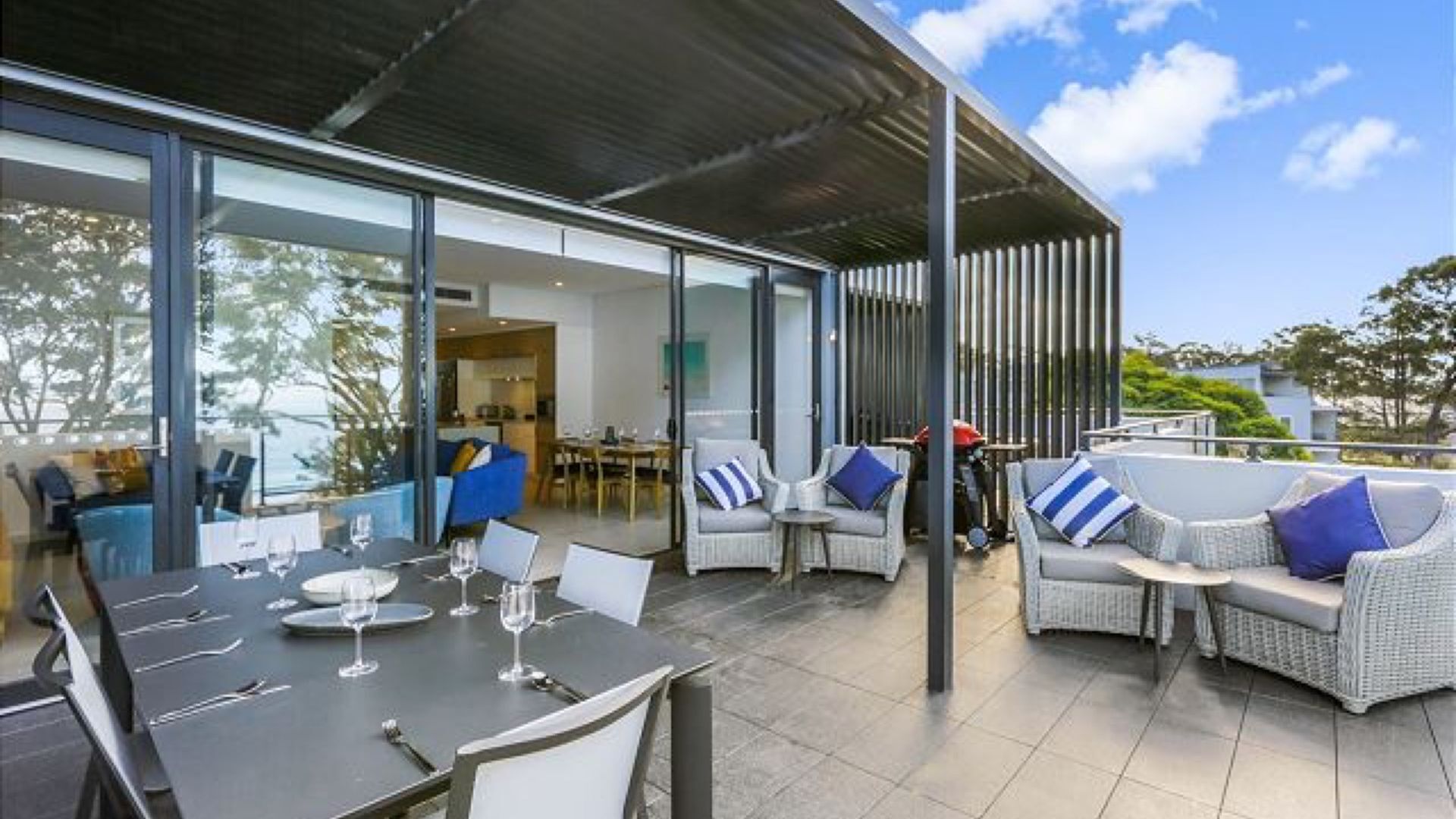 A modern outdoor dining area with a glass-enclosed patio, wicker furniture, and a view of the surrounding landscape.
