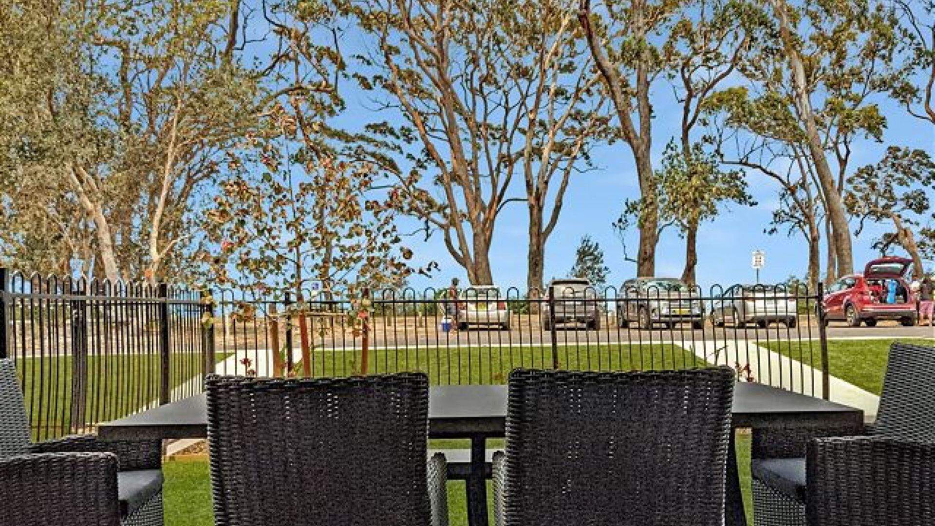 An outdoor seating area with wicker furniture and a view of trees and parked cars.