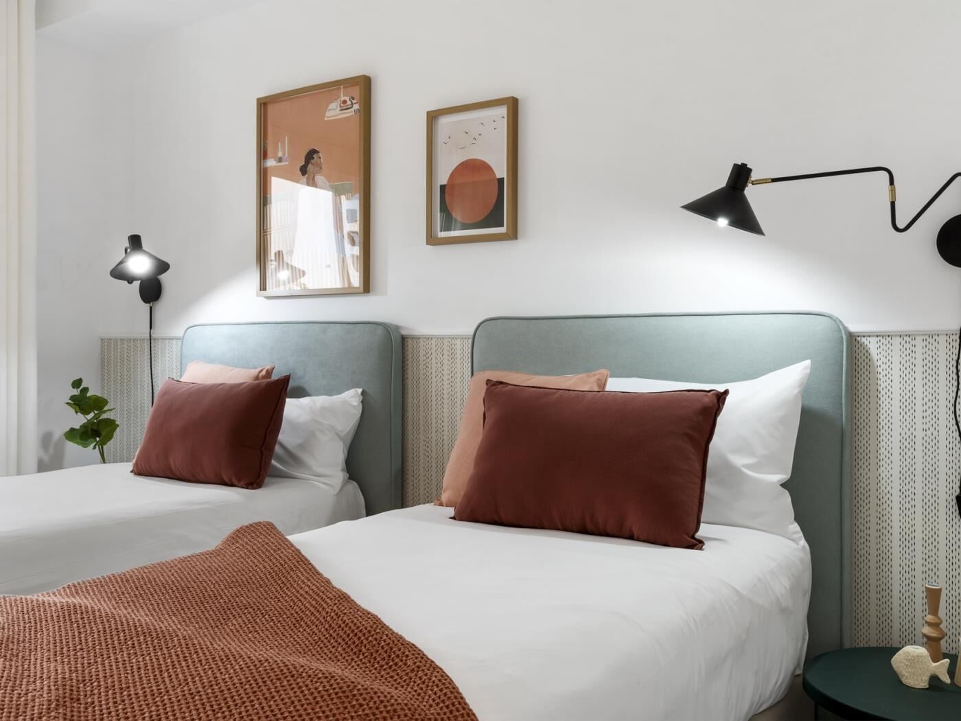 Hotellihuone, jossa on kaksi sänkyä, suuri ikkuna, seinään kiinnitetty valaisin ja kaksi kehystettyä kuvaa.