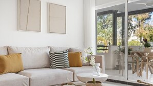 Ett modernt vardagsrum med en beige soffa, ett soffbord med dekorativa föremål och utsikt över en balkong med utemöbler.