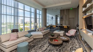A spacious lounge area with large windows, a seating arrangement including sofas and chairs, a coffee table, and a bar area in the background. - Hollywood Beach HHouse Rentals (Hollywood)