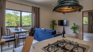 Een moderne keuken met een gasfornuis, een eettafel met een schaal fruit, en een blauwe bank.