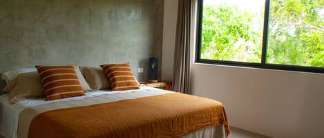 A bedroom with a large window, a bed with a brown blanket, and a concrete wall.